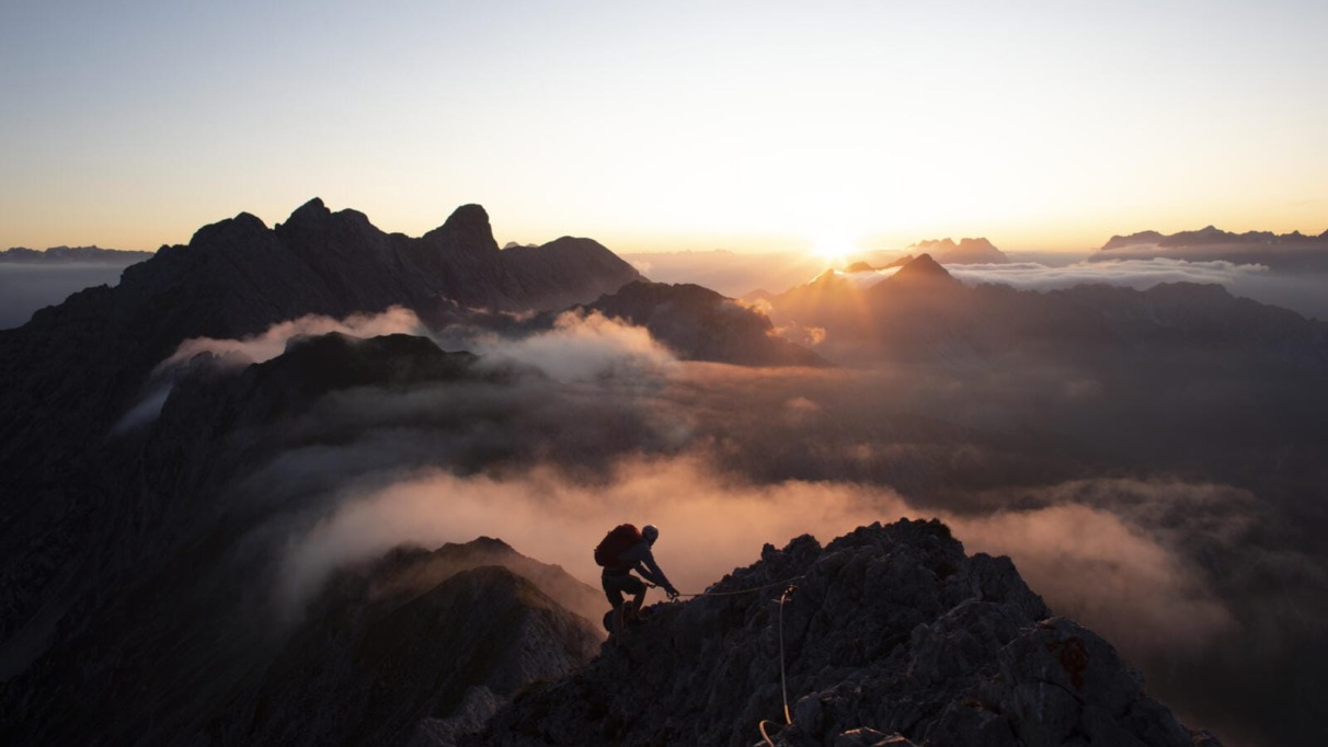 Bergsporter klimt bij zonsopkomst door de Alpen in Tirol