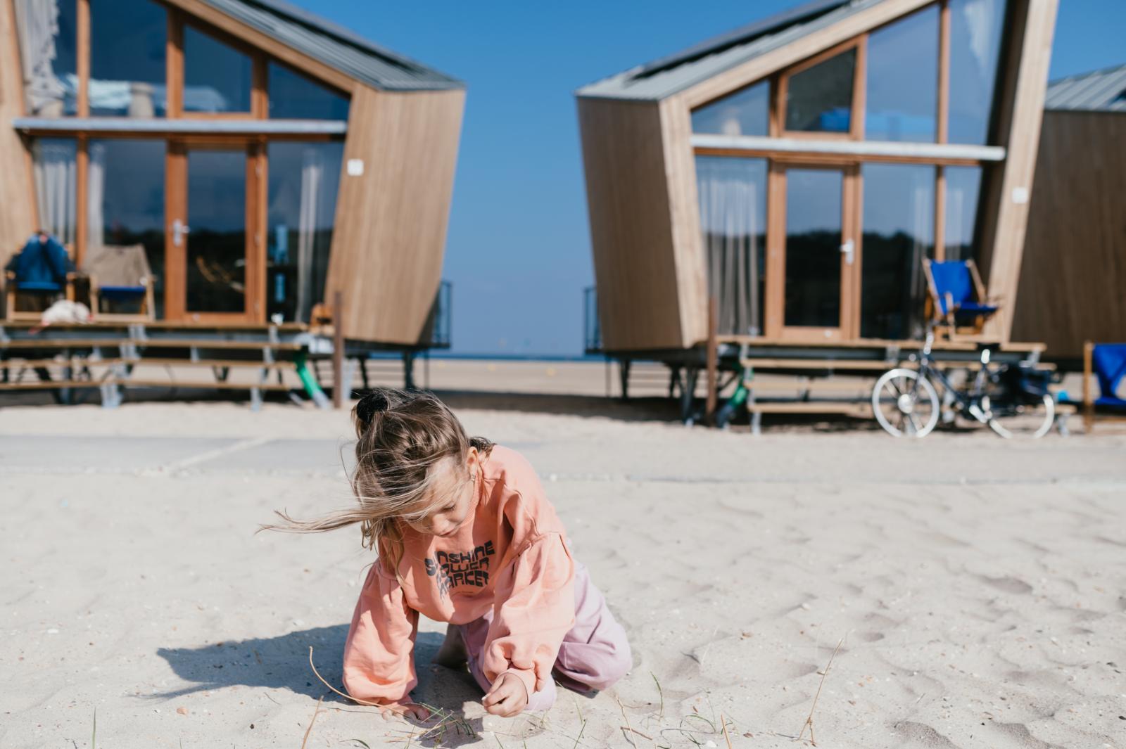 Kind speelt in het zand voor de moderne houten strandhuisjes van Breezand in Vrouwenpolder, Zeeland.