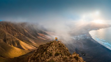 Stel staat bovenop een klif om naar de zonsondergang te kijken op Lanzarote, Canarische eilanden