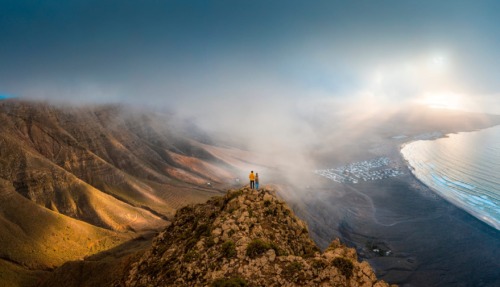Stel staat bovenop een klif om naar de zonsondergang te kijken op Lanzarote, Canarische eilanden