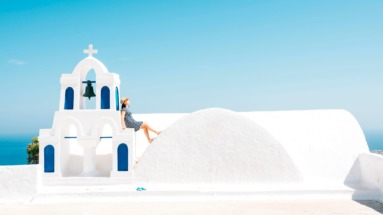 Vrouw leunt op kapelletje in Oia, Santorini, Griekenland