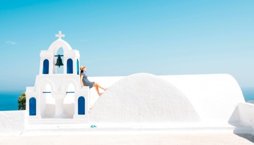 Vrouw leunt op kapelletje in Oia, Santorini, Griekenland