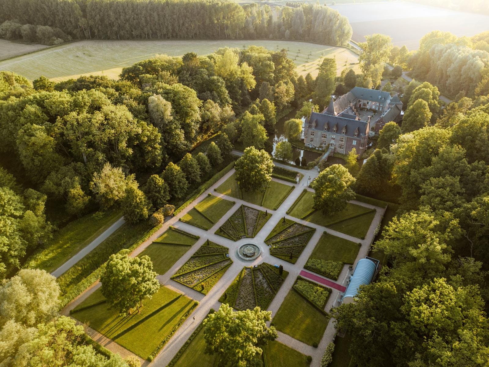 Luchtfoto van Kasteel TerWorm in Heerlen, omringd door een symmetrische kasteeltuin en uitgestrekte bossen bij zonsondergang.