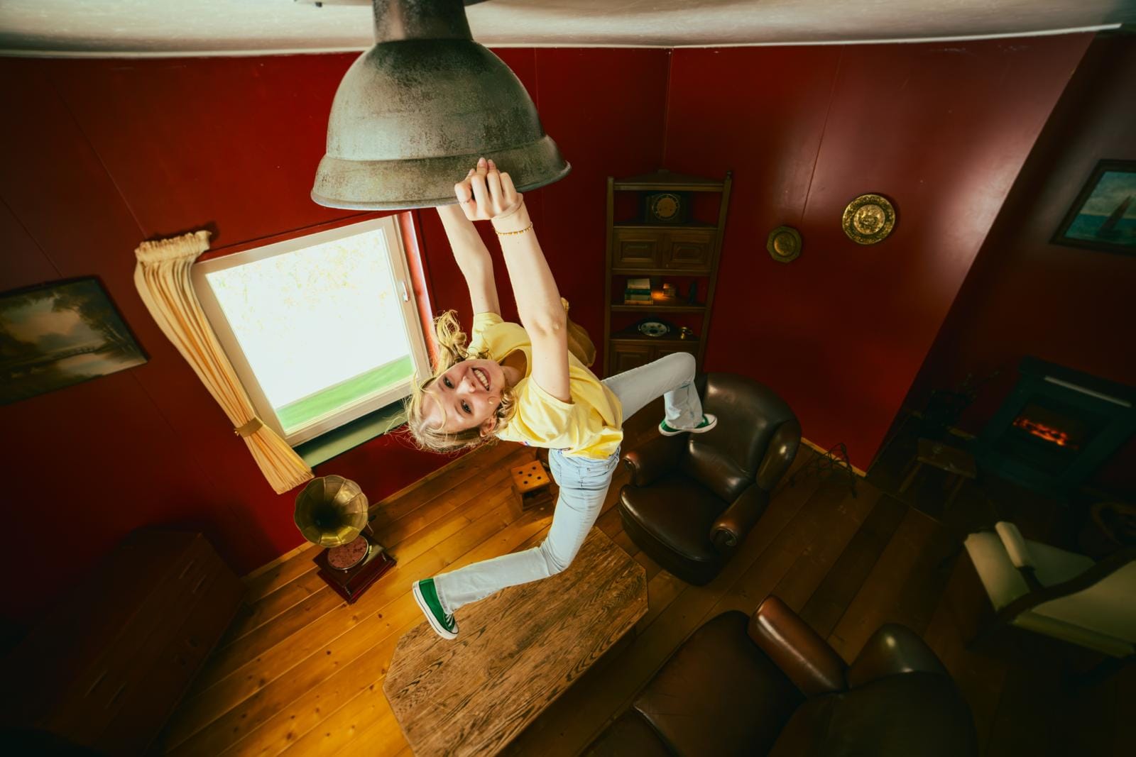 Meisje hangt lachend aan een lamp in een omgekeerde kamer in belevingsmuseum Mind Mystery in Horst