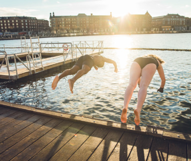 Twee vrienden van verschillende leeftijd en afkomst die in Kopenhagen, Denemarken in koud water springen