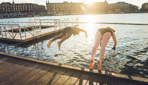 Twee vrienden van verschillende leeftijd en afkomst die in Kopenhagen, Denemarken in koud water springen