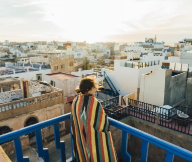 Vrouw met kleurrijke deken kijkt uit over de dakterrassen van de medina in Essaouira, Marokko