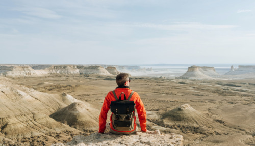 Hiker met rugzak zit bovenop berg en kijkt uit over Bszhira Canyon, Kazachstan