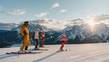 Familie skiet bij zonsopkomst op de pistes van de Tiroler Zugspitz Arena met uitzicht op de Alpen