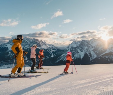 Familie skiet bij zonsopkomst op de pistes van de Tiroler Zugspitz Arena met uitzicht op de Alpen