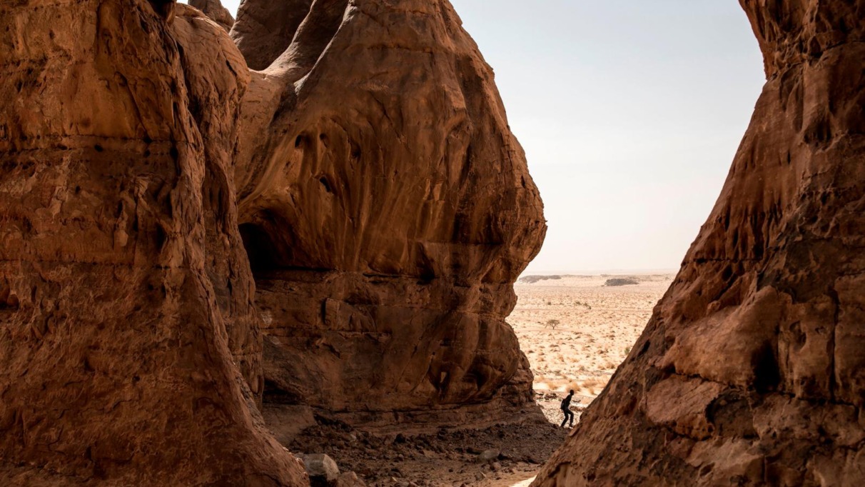 Man wandelt tussen imposante rode rotsformaties in de Adrar-woestijn van Mauritanië.