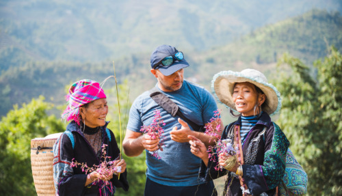 white european male tourist standing together with two indigenous woman from the black hmong tribe in the sapa mountains in vietnam, holding wild flowers in hands and talking