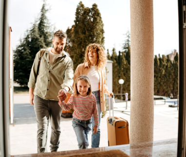 Blije familie voor een huis met een koffer