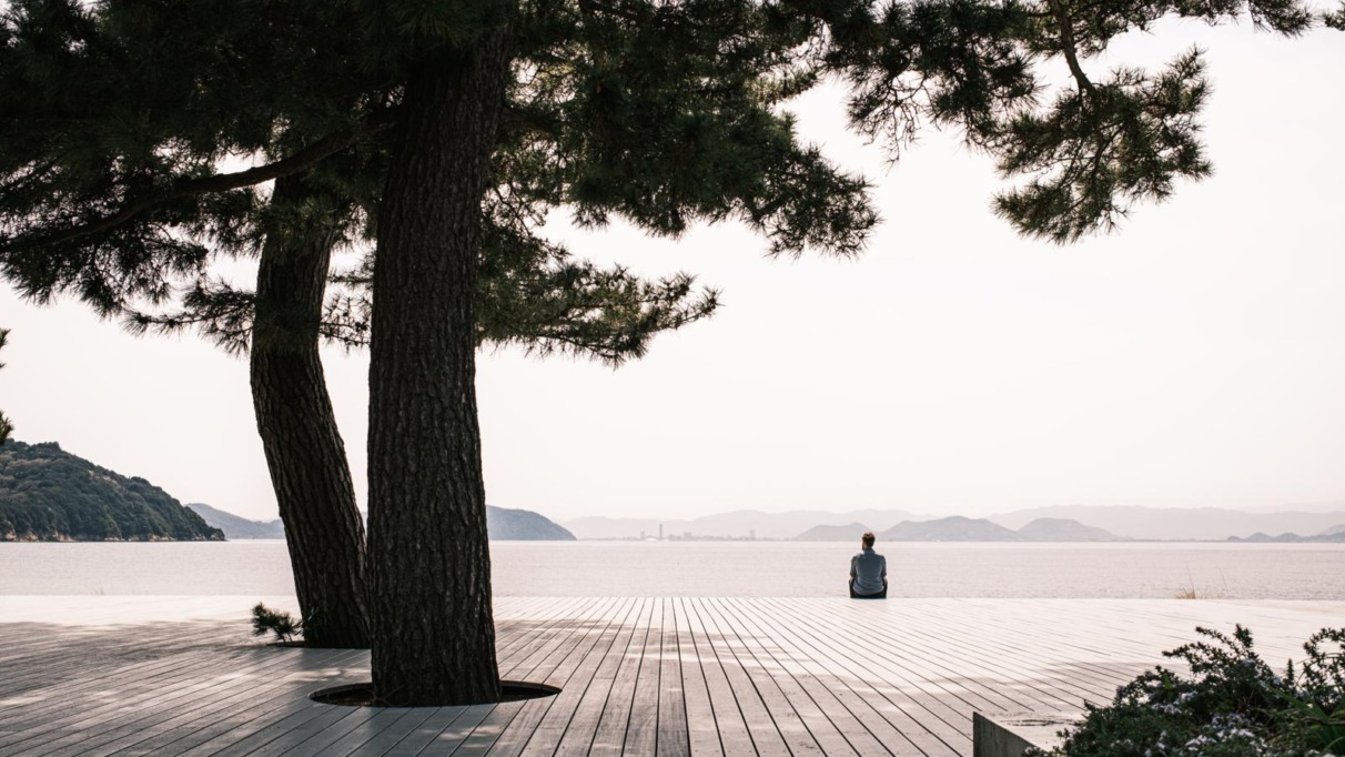 Persoon zit alleen op een houten platform aan zee op Naoshima, het kunsteiland van Japan.