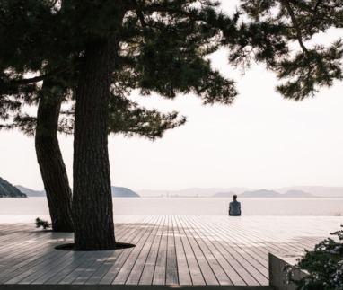 Persoon zit alleen op een houten platform aan zee op Naoshima, het kunsteiland van Japan.