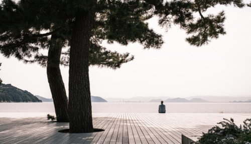 Persoon zit alleen op een houten platform aan zee op Naoshima, het kunsteiland van Japan.
