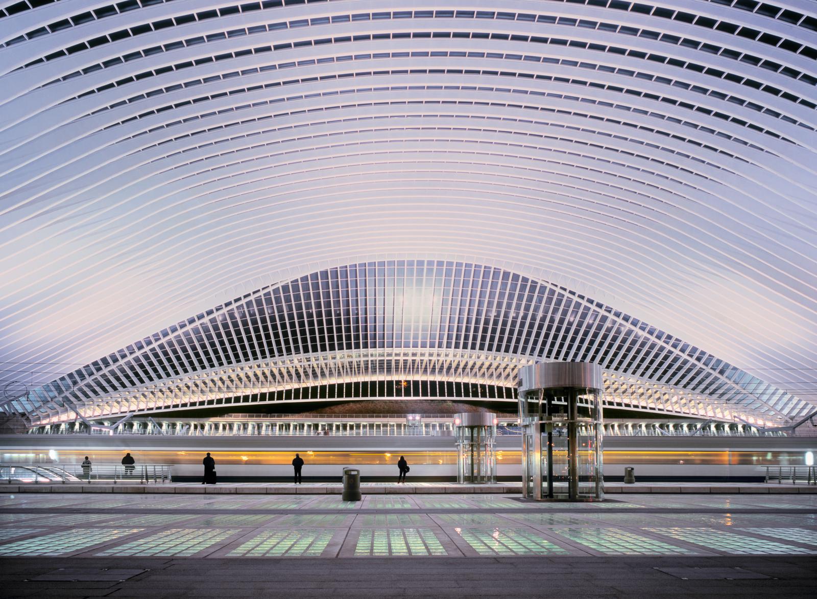 Modern treinstation Luik-Guillemins met gebogen glazen dak bij avondlicht.