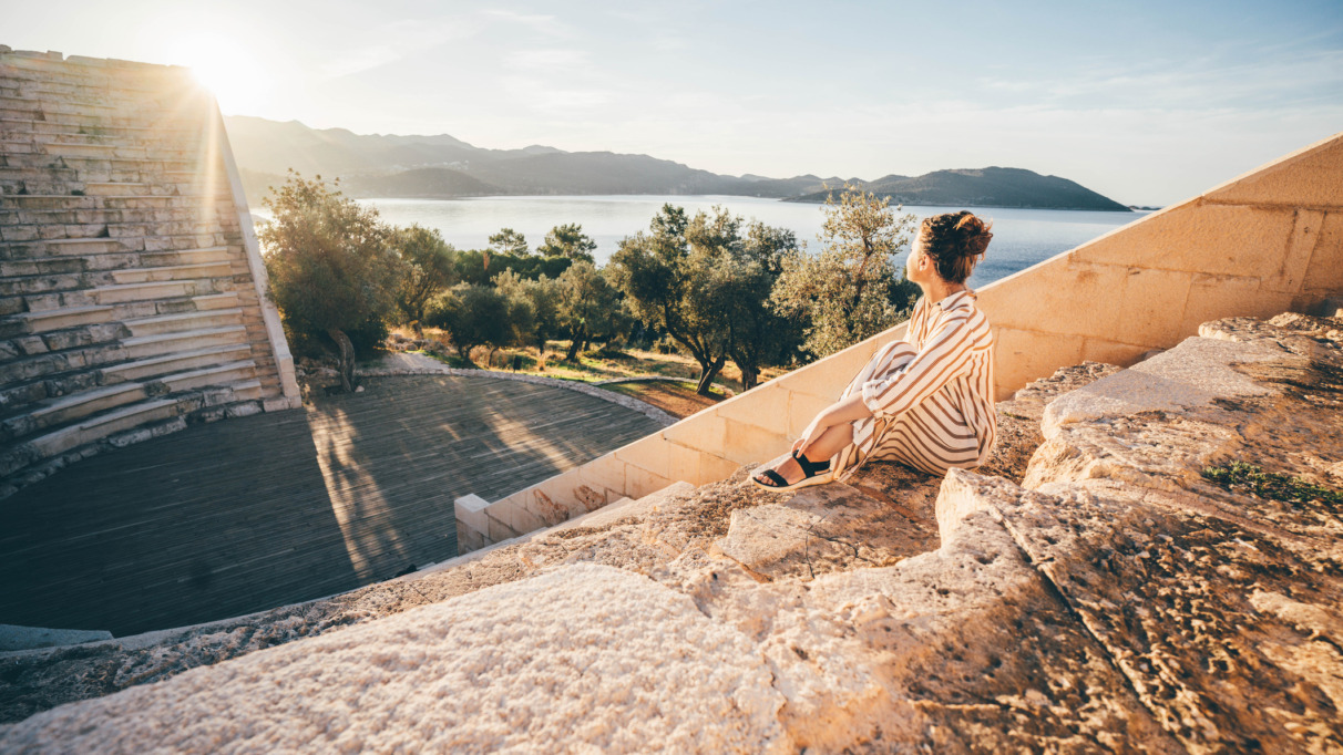 Reiziger geniet van zonsondergang in het antieke theater van Kaş met uitzicht op de Middellandse Zee, Turkije