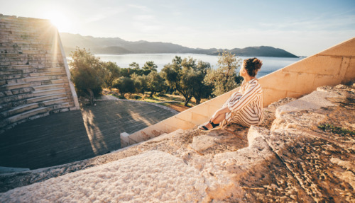 Reiziger geniet van zonsondergang in het antieke theater van Kaş met uitzicht op de Middellandse Zee, Turkije