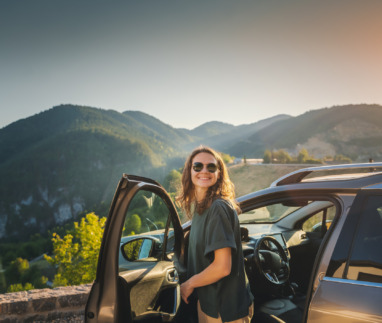 Jonge vrouw stapt auto uit in de bergen van Europa op zonnige dag