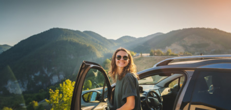 Jonge vrouw stapt auto uit in de bergen van Europa op zonnige dag