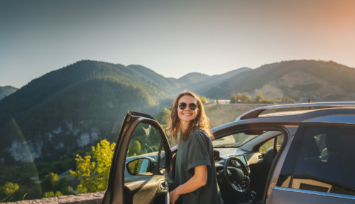 Jonge vrouw stapt auto uit in de bergen van Europa op zonnige dag
