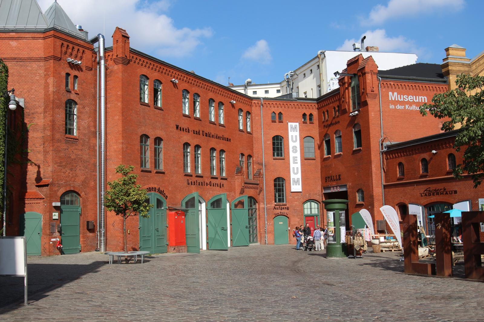 Binnenplaats van de Kulturbrauerei in Berlijn met rode bakstenen gebouwen en museumborden.