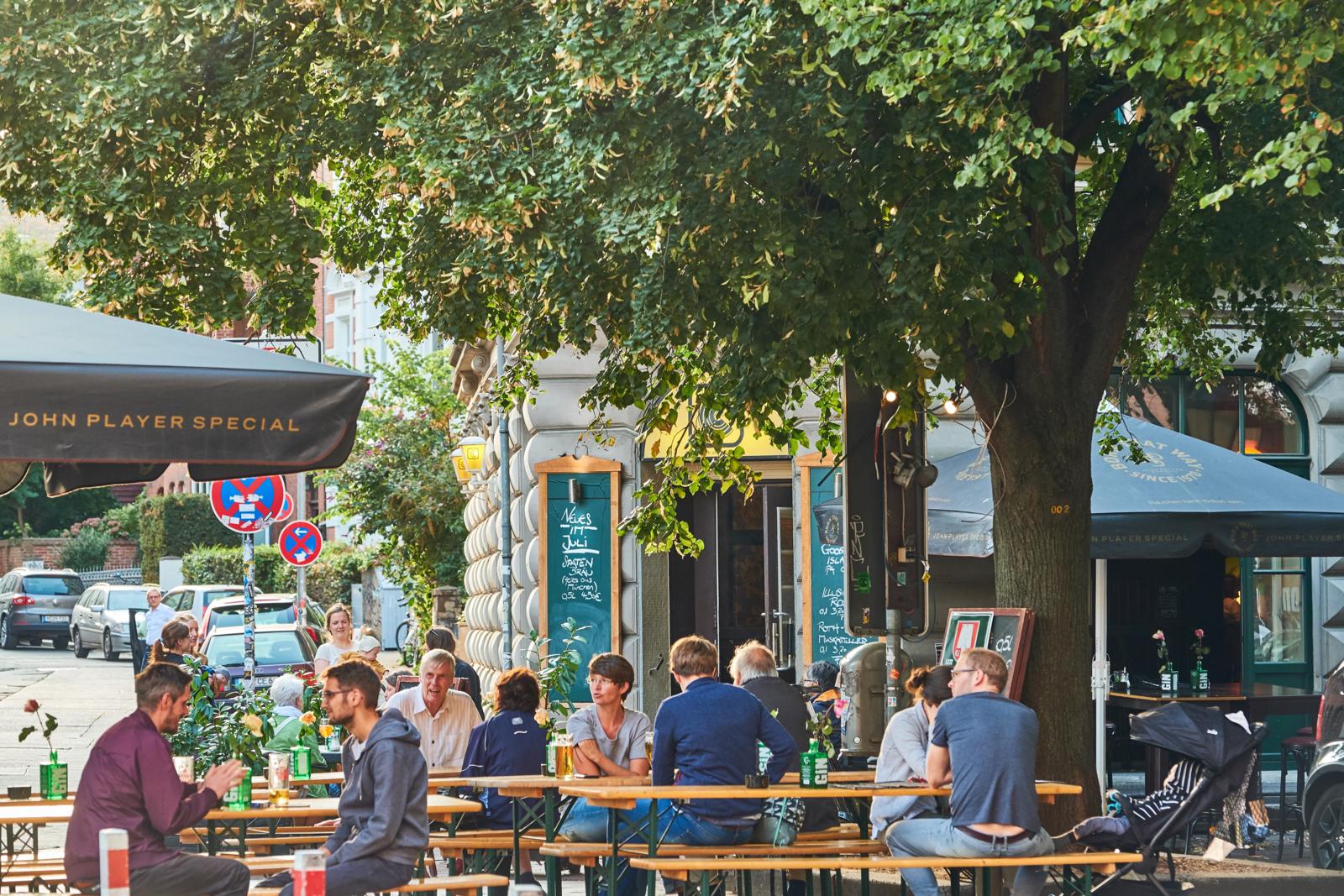 Mensen op een zonnig terras onder de bomen in de levendige wijk Linden in Hannover.