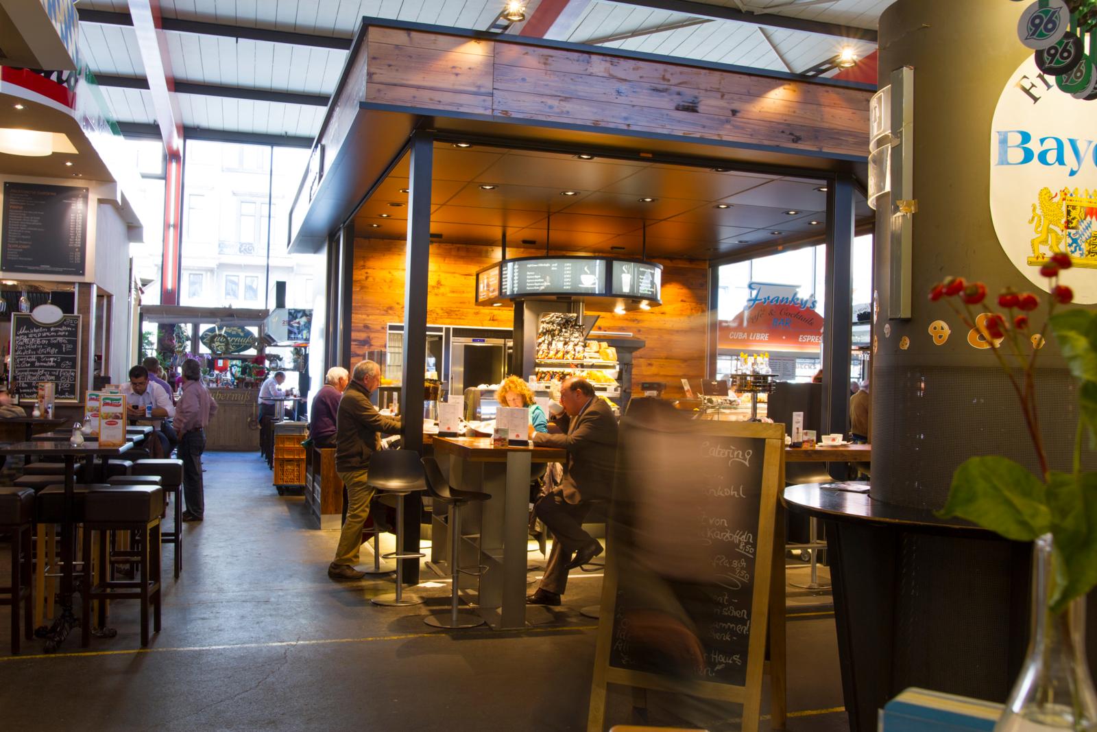 Binnenaanzicht van de Markthalle in Hannover met locals aan tafeltjes en een koffiebar.