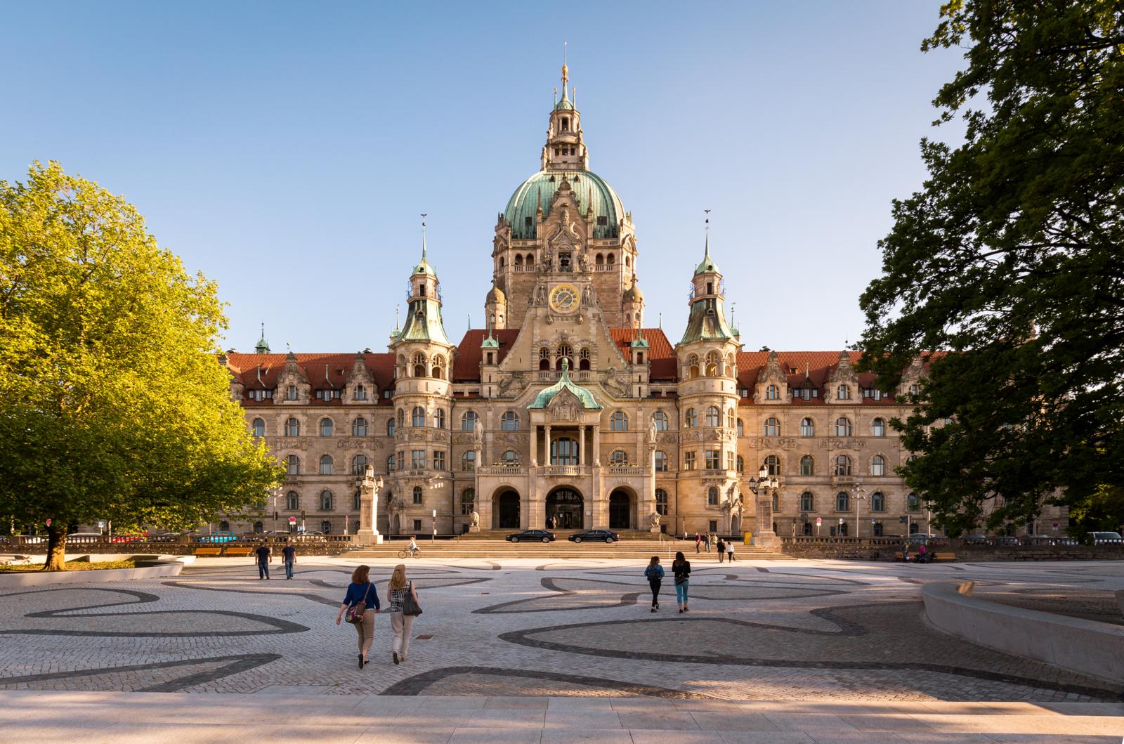Voorzijde van het Neues Rathaus in Hannover bij helder weer met mensen op het plein.