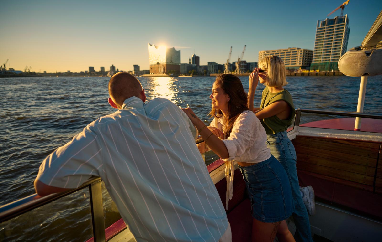 Drie mensen genieten van de zonsondergang tijdens een boottocht over de Elbe in Hamburg met uitzicht op de Elbphilharmonie.