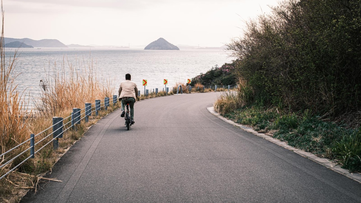 Fietser op een kustweg op Naoshima, Japan, met uitzicht op zee en kleine eilanden aan de horizon