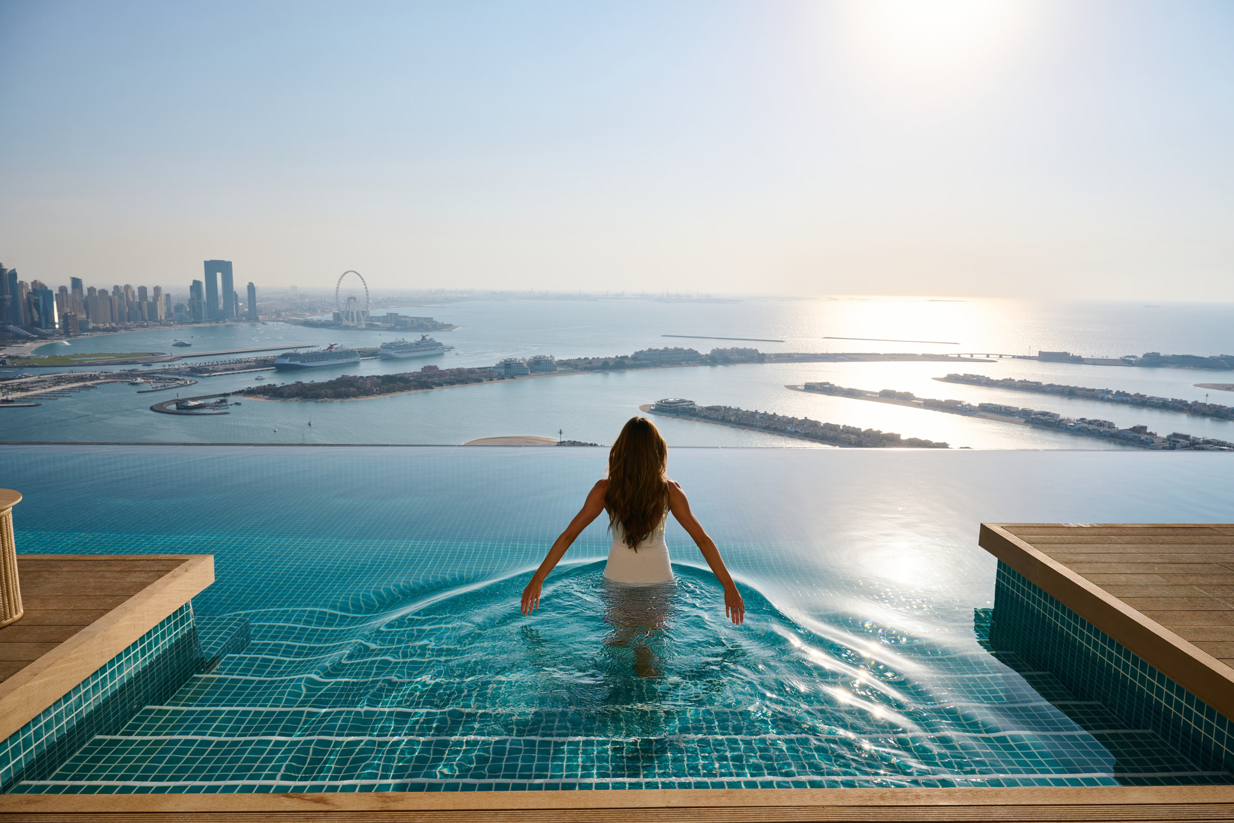 Vrouw in infinity pool met uitzicht op Dubai en de Palm.