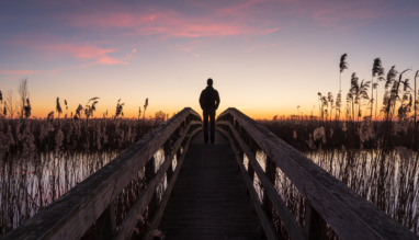 Man staat tijdens zonsondergang op een smalle brug tussen het riet