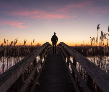 Man staat tijdens zonsondergang op een smalle brug tussen het riet