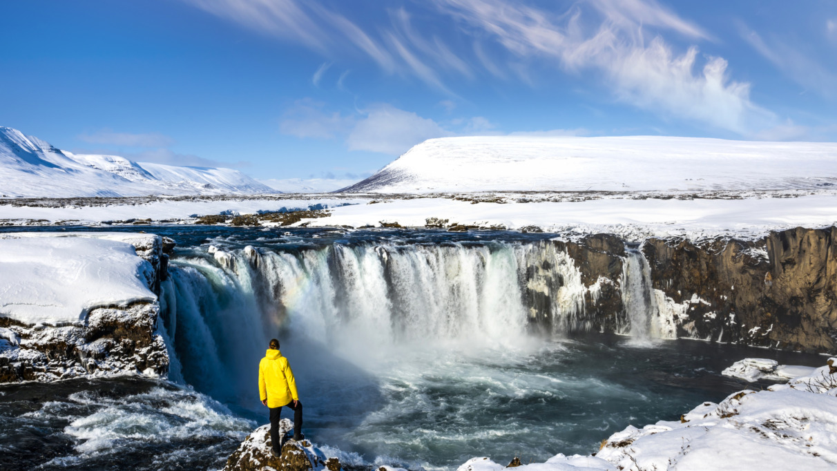 Man in gele jas bij de Godafoss-waterval in IJsland