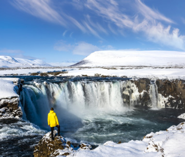 Man in gele jas bij de Godafoss-waterval in IJsland