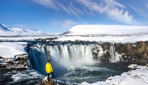 Man in gele jas bij de Godafoss-waterval in IJsland