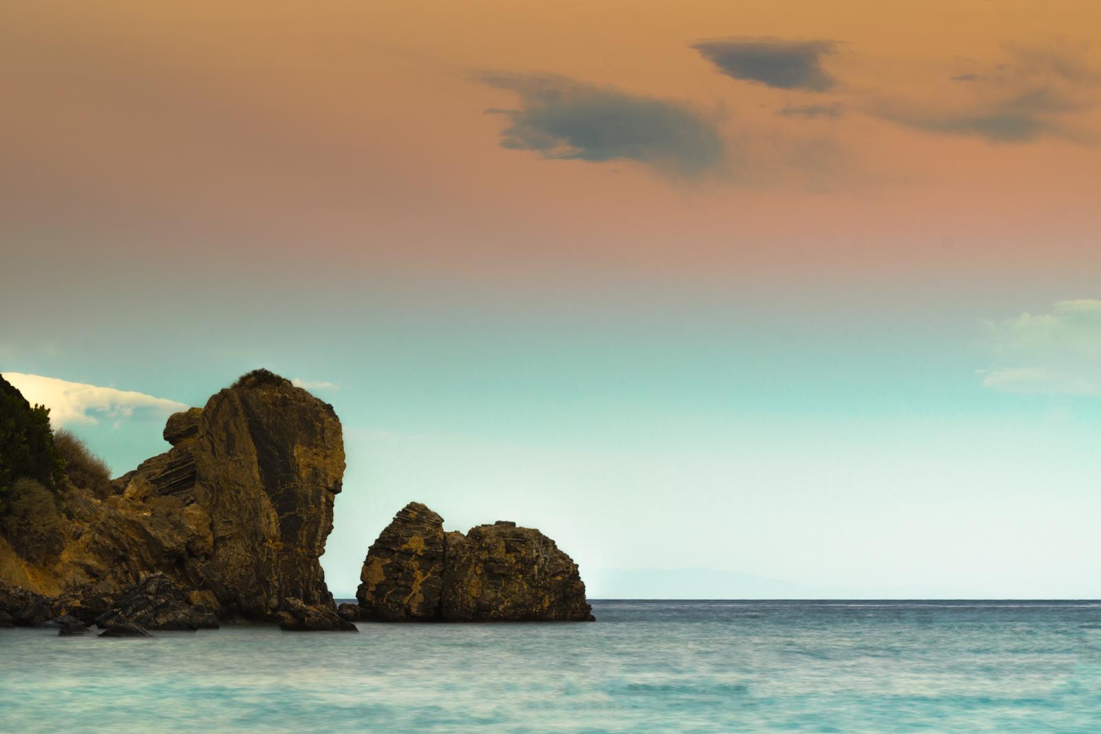 Rotsformaties in zee langs de Griekse kust bij kleurrijke zonsondergang.
