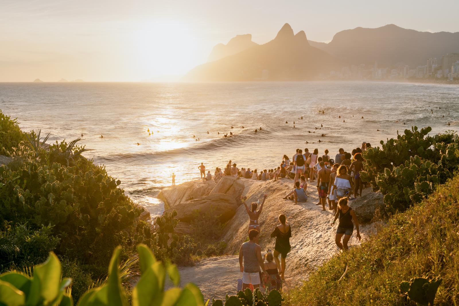 Mensen genieten van de zonsondergang bij Ipanema Beach in Rio de Janeiro met surfers in de golven.