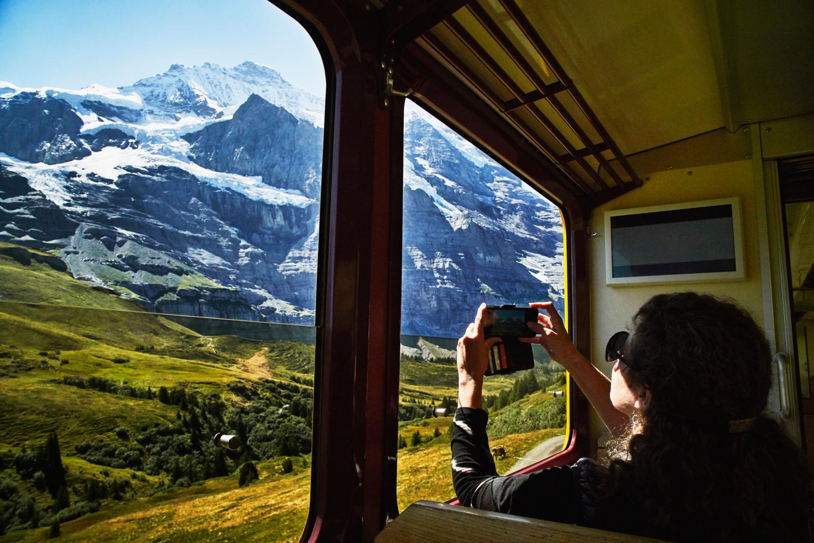 Vrouw fotografeert de besneeuwde Jungfrau-berg vanuit een Zwitserse panoramatrein.