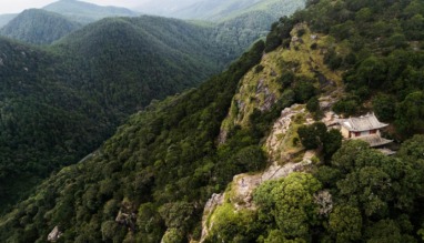 Luchtfoto van een afgelegen tempel op een bergrug bij Shaxi in Yunnan, China, omgeven door dichtbegroeide groene heuvels