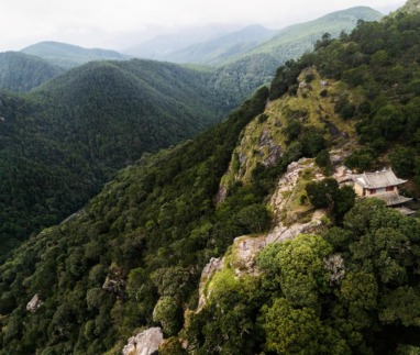 Luchtfoto van een afgelegen tempel op een bergrug bij Shaxi in Yunnan, China, omgeven door dichtbegroeide groene heuvels