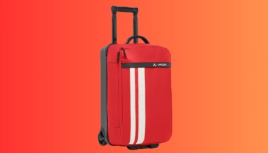 Rode duurzame reiskoffer van Vaude met wielen en uittrekbare handgreep op oranje achtergrond