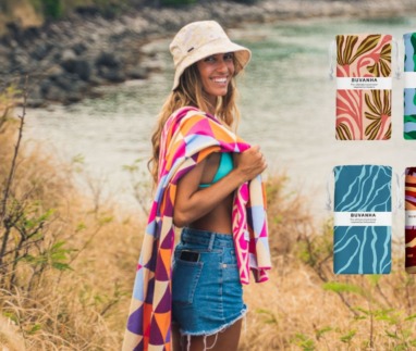 Vrouw met kleurrijke Buvanha-handdoek bij het water, met verschillende dessins van duurzame strandhanddoeken