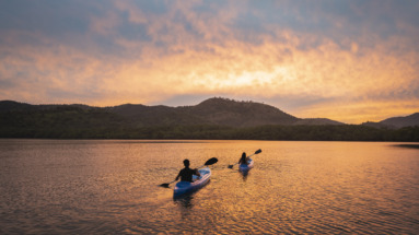 Twee mensen kajakken bij zonsondergang