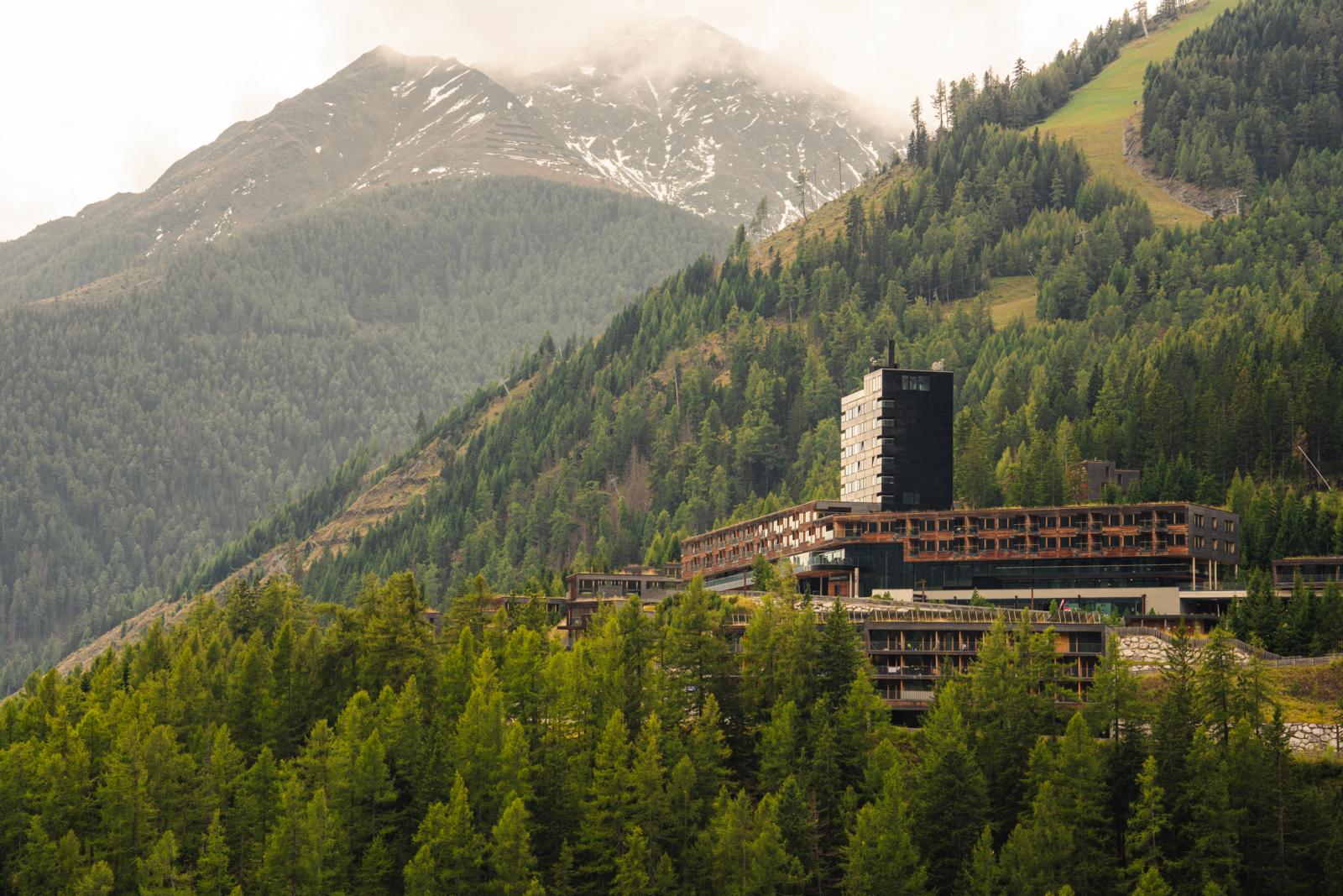 Modern bergresort tussen de dennenbossen van Oost-Tirool met hoge pieken op de achtergrond.