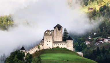 Middeleeuwse burcht op een heuveltop in Tirol met mist rond de bergen.