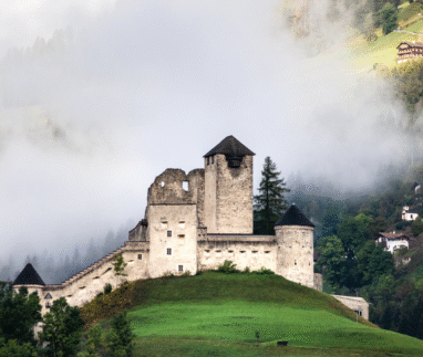 Middeleeuwse burcht op een heuveltop in Tirol met mist rond de bergen.