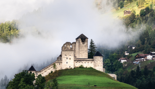 Middeleeuwse burcht op een heuveltop in Tirol met mist rond de bergen.
